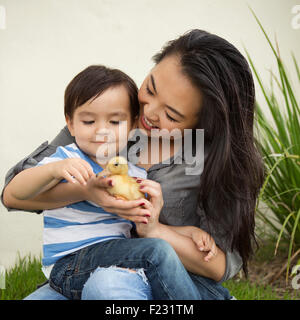 Lächelnde Frau hält eine gelbe Entlein in ihren Händen, ihrem kleinen Sohn beobachten. Stockfoto