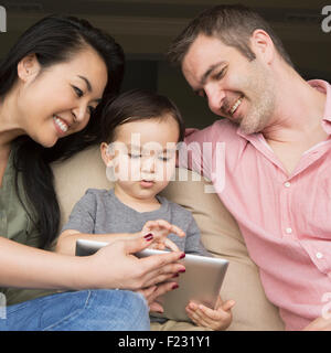 Eltern sitzen auf einem Sofa mit ihrem jungen Sohn, Blick auf eine digital-Tablette. Stockfoto