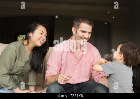 Lächeln Mann und Frau sitzen nebeneinander auf dem Sofa, spielt mit ihren kleinen Sohn. Stockfoto