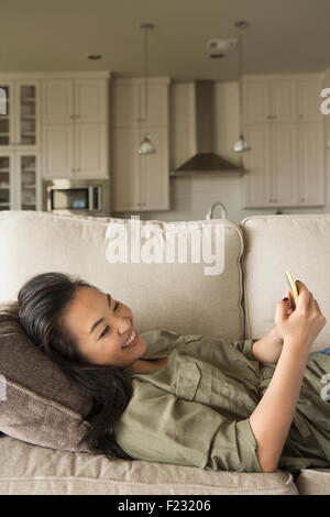 Frau liegt auf dem Sofa, Lächeln, einen Blick auf ein Handy. Stockfoto