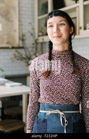 Eine Frau mit Zöpfen trägt eine Schürze, eine Kellnerin in einem Restaurant. Stockfoto