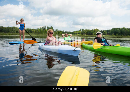 Familie der älteren Frau mit drei erwachsenen Kindern sind paddeln Kajaks und Paddleboards über einen See im Norden von Minnesota Stockfoto