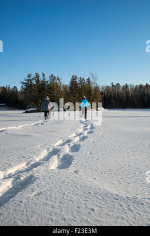 Erwachsene Frauen, die über einen gefrorenen Schnee See in Ely, Minnesota an einem kalten Schneeschuhwandern unter Null Temperatur Winter Tag hinterlassen Spuren Stockfoto