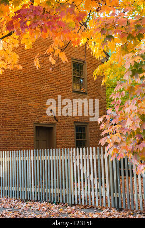 Herbst-Szene mit Orange-gelben Blätter an einem Ahornbaum in der Nähe ein Backsteingebäude und Zaun in winzigen New Harmony, IN, USA Stockfoto