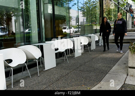 Zwei junge Frauen, die zu Fuß durch weiße Outdoor-Café-Tischen in der Innenstadt von Vancouver, BC, Kanada Stockfoto