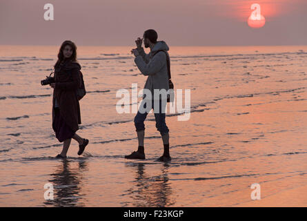 Silhouetten bei Ebbe. Der Strand, Brighton and Hove, England. Paar mit Kameras Stockfoto