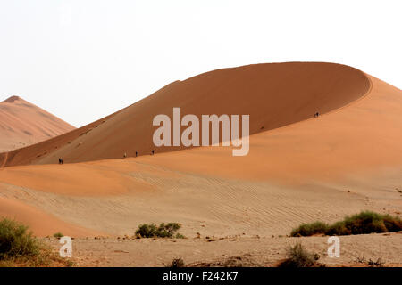 Touristen machen den langen Aufstieg an die Spitze der auf riesigen Dünen im Sossusvlei, Namib-Wüste, Namibia. Stockfoto