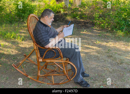 Ältere Mann tut Skizze beim Sitzen in einer Korb-Schaukelstuhl Stockfoto