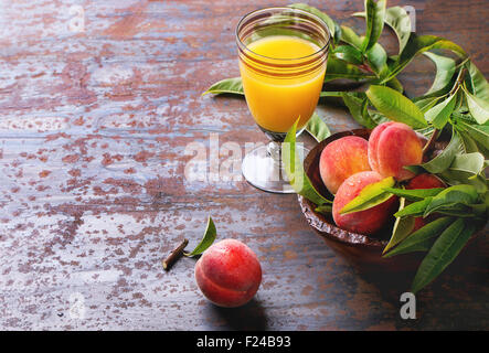 Pfirsiche auf Zweig mit Blättern in Holzschale und Glas mit Pfirsich Saft über alte Metall Hintergrund. Stockfoto