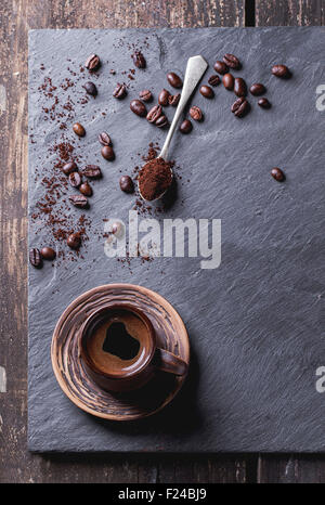 Braune Keramik Tasse frischen Kaffee, Tee-Löffel mit Kaffeepulver und Kaffeebohnen über schwarzen Schiefer als Hintergrund. Mit Textfreiraum Stockfoto