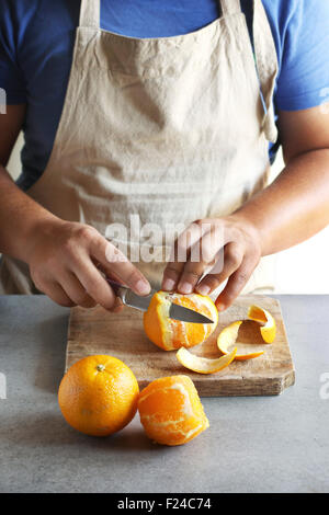 Mann schälen einer Orange mit einem Messer in einer Küche-board Stockfoto