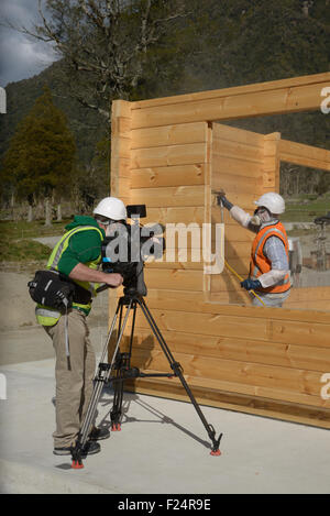 Ein Dokumentarfilmer filmt ein Kaufmann Spritzlackierung der Wand eine hölzerne Industriegebäude mit Holz-Konservierungsmittel Stockfoto