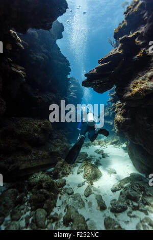 Taucher schwimmt durch einen schmalen Durchgang in einem Korallenriff Stockfoto