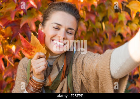 Portrait von glücklich entspannt Frau mit Herbst Blätter vor Laub machen selfie Stockfoto