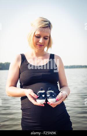 Porträt einer jungen und schönen schwangeren Frau hält kleine Schuhe ihres zukünftigen Kindes. Stockfoto