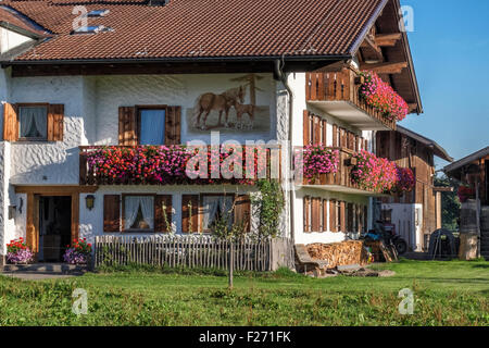 Typisch bayerisches Bauernhaus mit hölzernen Fensterläden, Fenster, Blumentöpfe und Wandmalerei der Pferde, Bayern, Deutschland Stockfoto