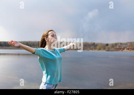 Sommersprossige fröhliches Mädchen mit ausgestreckten Armen lächelnd zu Sonne und schließen ihre Augen Stockfoto