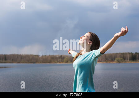 Sommersprossige fröhliches Mädchen mit ausgestreckten Armen lächelnd zu Sonne und schließen ihre Augen Stockfoto