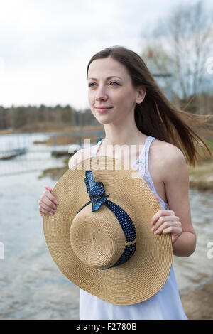 Sommersprossige glückliches Mädchen im weißen Kleid Stroh Hut in den Händen hält und wegsehen bei windigem Wetter Stockfoto