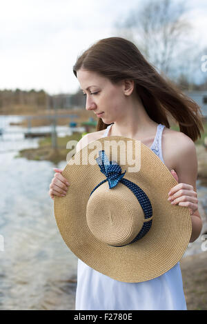 Sommersprossige glückliches Mädchen im weißen Kleid Stroh Hut in den Händen hält und Blick auf die Seite bei windigem Wetter Stockfoto