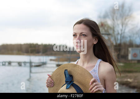 Sommersprossige glückliches Mädchen im weißen Kleid Stroh Hut in den Händen hält und wegsehen bei windigem Wetter Stockfoto