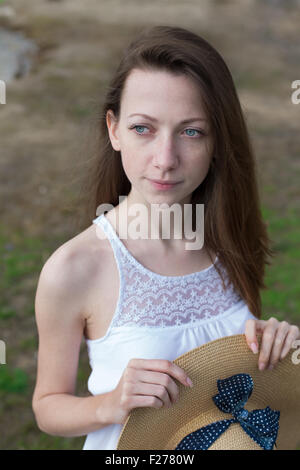 Sommersprossige glückliches Mädchen im weißen Kleid Stroh Hut in ihren Händen hält und wegsehen bei windigem Wetter Stockfoto