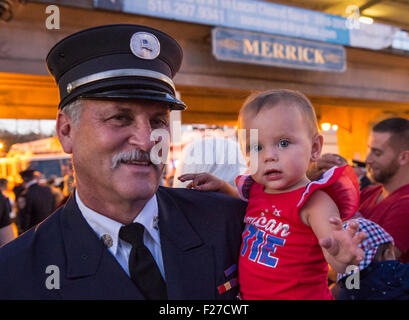 Merrick, New York, USA. 11. September 2015. RILEY E. GIES, ist ein-jährige Enkelin von Feuerwehrchef Ronnie E Gies verstorbenen Reaktion auf 9/11 NYC Terrorist Attack, hielt von CRAIG MALTZ, ein Freiwilliger Feuerwehrmann Bellmore, nachdem Merrick Gedenkfeier für Merrick Freiwillige Feuerwehr und Bewohner, die aufgrund von 9/11 Terroranschlag in New York City Twin Towers gestorben. Bildnachweis: Ann E Parry/Alamy Live-Nachrichten Stockfoto