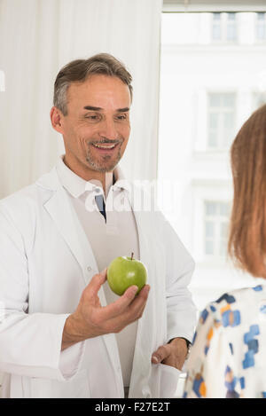 Männlichen Arzt bietet einen Apfel für Patienten in seiner Klinik, München, Bayern, Deutschland Stockfoto