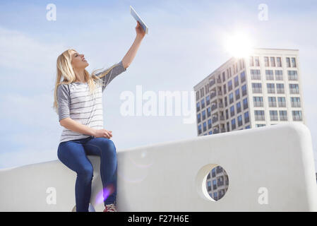 Teenager-Mädchen sitzen auf einer Mauer und nehmen Selfie mit digital-Tablette, München, Bayern, Deutschland Stockfoto