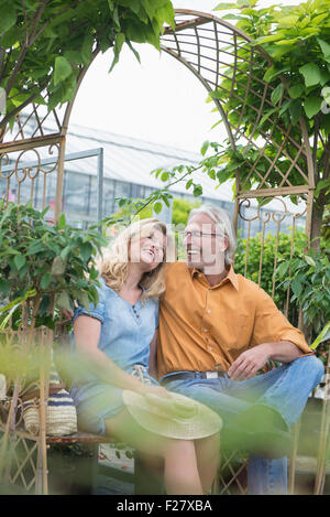 Älteres Paar auf einer Bank sitzen und lächelnd in Gärtnerei, Augsburg, Bayern, Deutschland Stockfoto