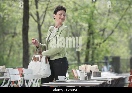 Reife Frau mit Handtasche, die auf der Suche über die Schulter in den Bürgersteig Café, Bayern, Deutschland Stockfoto