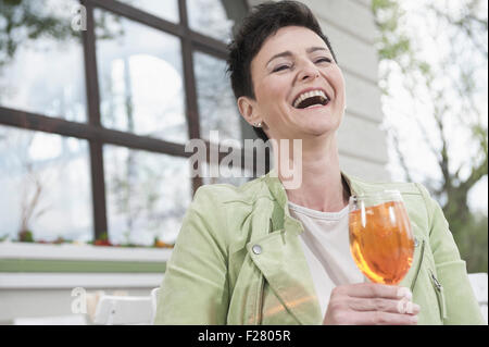 Reife Frau lachend mit Aperol Spritzat am Bürgersteig Café, Bayern, Deutschland Stockfoto