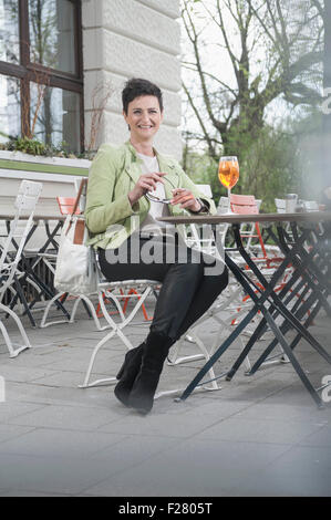 Reife Frau trinken Aperol Spritzat am Bürgersteig Café, Bayern, Deutschland Stockfoto