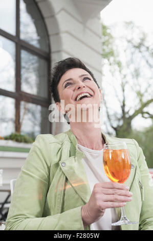 Reife Frau lachend mit Aperol Spritzat am Bürgersteig Café, Bayern, Deutschland Stockfoto