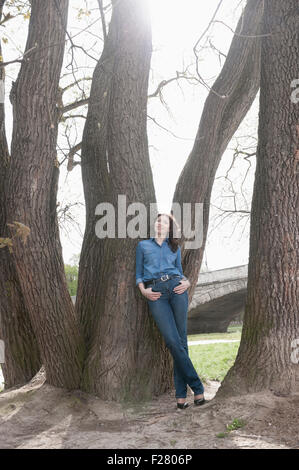 Reife Frau lehnte sich gegen Baum im Park, Bayern, Deutschland Stockfoto