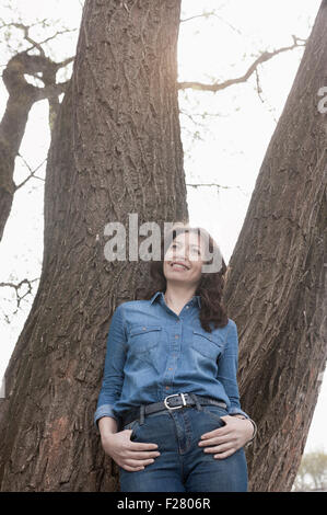 Reife Frau lehnte sich gegen Baum im Park, Bayern, Deutschland Stockfoto