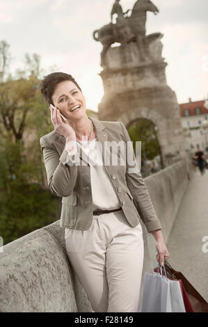 Reife Frau Telefonieren in Stadt mit Einkaufstüten, Bayern, Deutschland Stockfoto