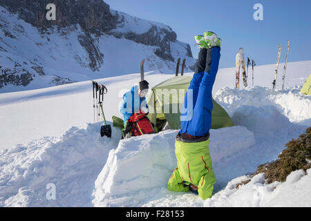 Mann beim Kopfstand Yoga im Camp, schneebedeckte Berge, Tirol, Österreich Stockfoto