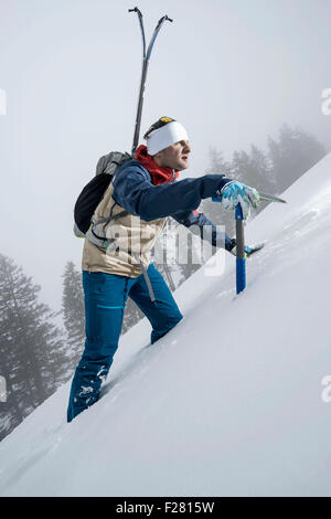 Männliche Bergsteiger hinauf verschneiten Hang mit Axt, Zell Am See, Österreich Stockfoto