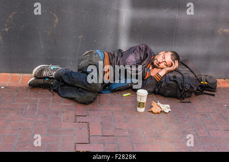 Eine 30er Jahre Obdachlosen Mann schläft, liegend, auf einem Bürgersteig in San Francisco. Er trägt eine Riesen-Hauptliga-Baseball-Jacke. Stockfoto