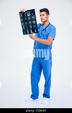 In voller Länge Portrait von einen schönen männlichen Arzt mit Blick auf Röntgen-Bild des Gehirns isoliert auf weißem Hintergrund Stockfoto