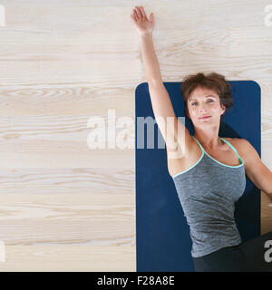 Draufsicht der Frau liegen und stretching auf Trainingsmatte. Frau Stock drehen ihren Körper und ihr einerseits Dehnung. Stockfoto