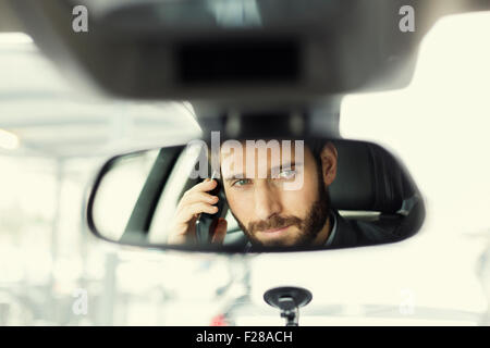 Fröhlicher Mensch auf Handy im Auto. Reflexion im Spiegel Stockfoto