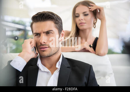 Porträt von ein gut aussehender Mann am Telefon im Freien im Restaurant im Gespräch mit Frau im Hintergrund Stockfoto
