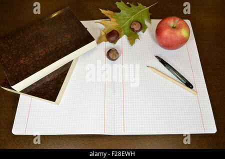 Geöffneten Notizbuch mit Bleistift, Kugelschreiber, Kastanien, welkes Blatt und Bücher auf hölzernen Schreibtisch - fallen Zusammensetzung Stockfoto