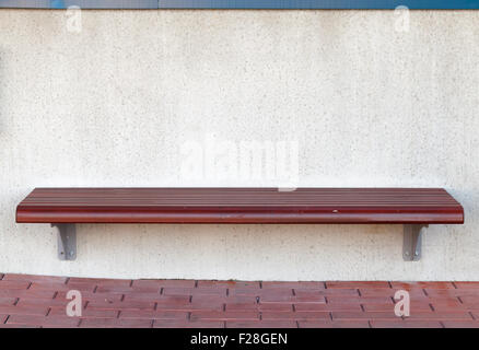 Hölzerne Straße Sitzbank montiert auf weißen Steinmauer an Bushaltestelle Stockfoto