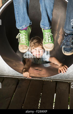 Junge, die Schiebetüren in einer Tunnelrutsche mit zwei Kindern baumelt ihre Füße, München, Bayern, Deutschland Stockfoto