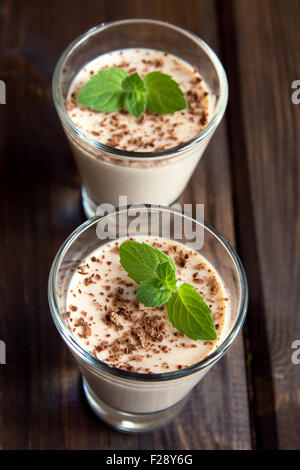 Panna Cotta Schokoladendessert mit Minze in Teil Brille auf dunklem Holz Stockfoto