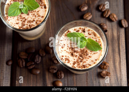 Panna Cotta Schokoladendessert mit Minze und Kaffeebohnen in Teil Brille auf dunklem Holz Stockfoto