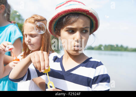 Mädchen bläst Seifenblasen mit Blase Zauberstäbe am Seeufer, Bayern, Deutschland Stockfoto